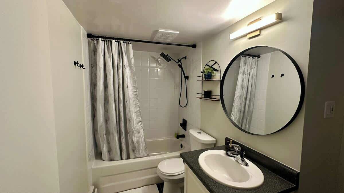 A bathroom with a bathtub, toilet, sink, shower, and a round mirror.