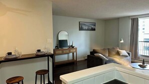 A modern living room with a sofa, a coffee table, a dining area with a table and chairs, and a large window with a view. - Urban Downtown Condo with Panoramic Views (Calgary)