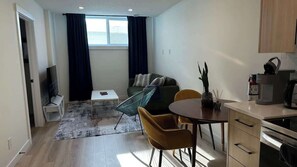A compact living space with a kitchenette, a dining area with chairs, a sofa, and a TV. - Modern Luxury Basement Suite (Calgary)