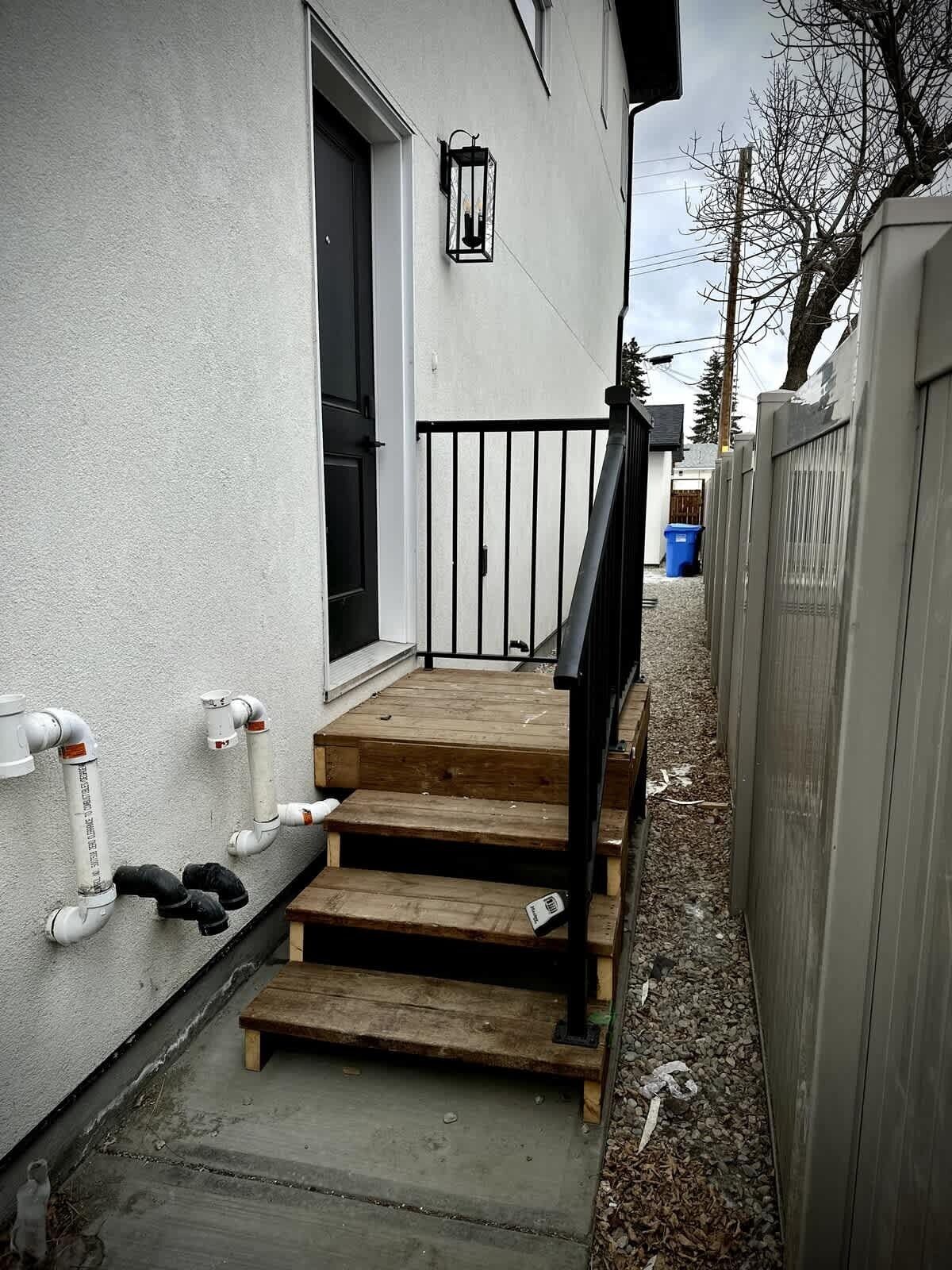 A residential property with a wooden staircase leading to a door, a black metal railing, and a white exterior wall with a black door.