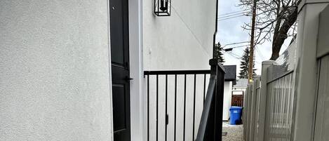 A residential property with a wooden staircase leading to a door, a black metal railing, and a white exterior wall with a black door.