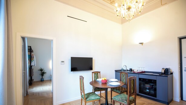 A dining area with a round table, chairs, a flat-screen TV, and a kitchen area with a stove and cabinets. - Luxury Boutique Apartment 3 in Palermo City Center, near the Central Station (Palermo)