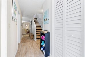 A hallway with wooden flooring, a staircase, and a shelf with folded towels. - Intracoastal Dock & Beach Access Townhome (St. Augustine)