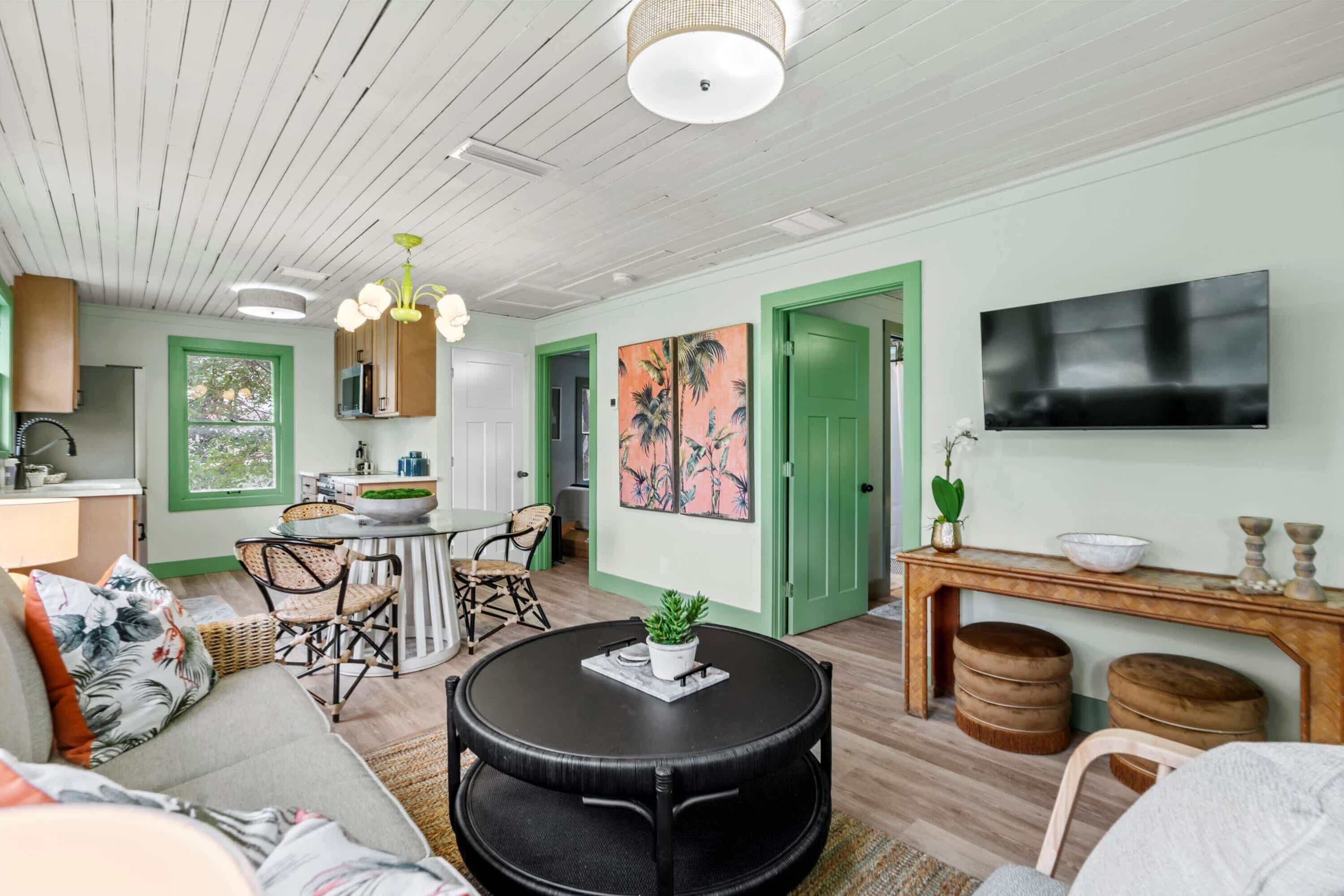 A cozy living room with a round black table, a sofa, and a dining area with a green door.