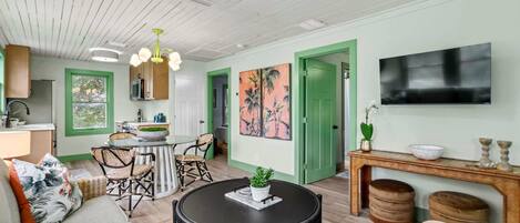 A cozy living room with a round black table, a sofa, and a dining area with a green door.