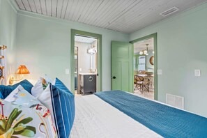 Ein Schlafzimmer mit Bett, Nachttisch, Lampe und Blick zum Essbereich.