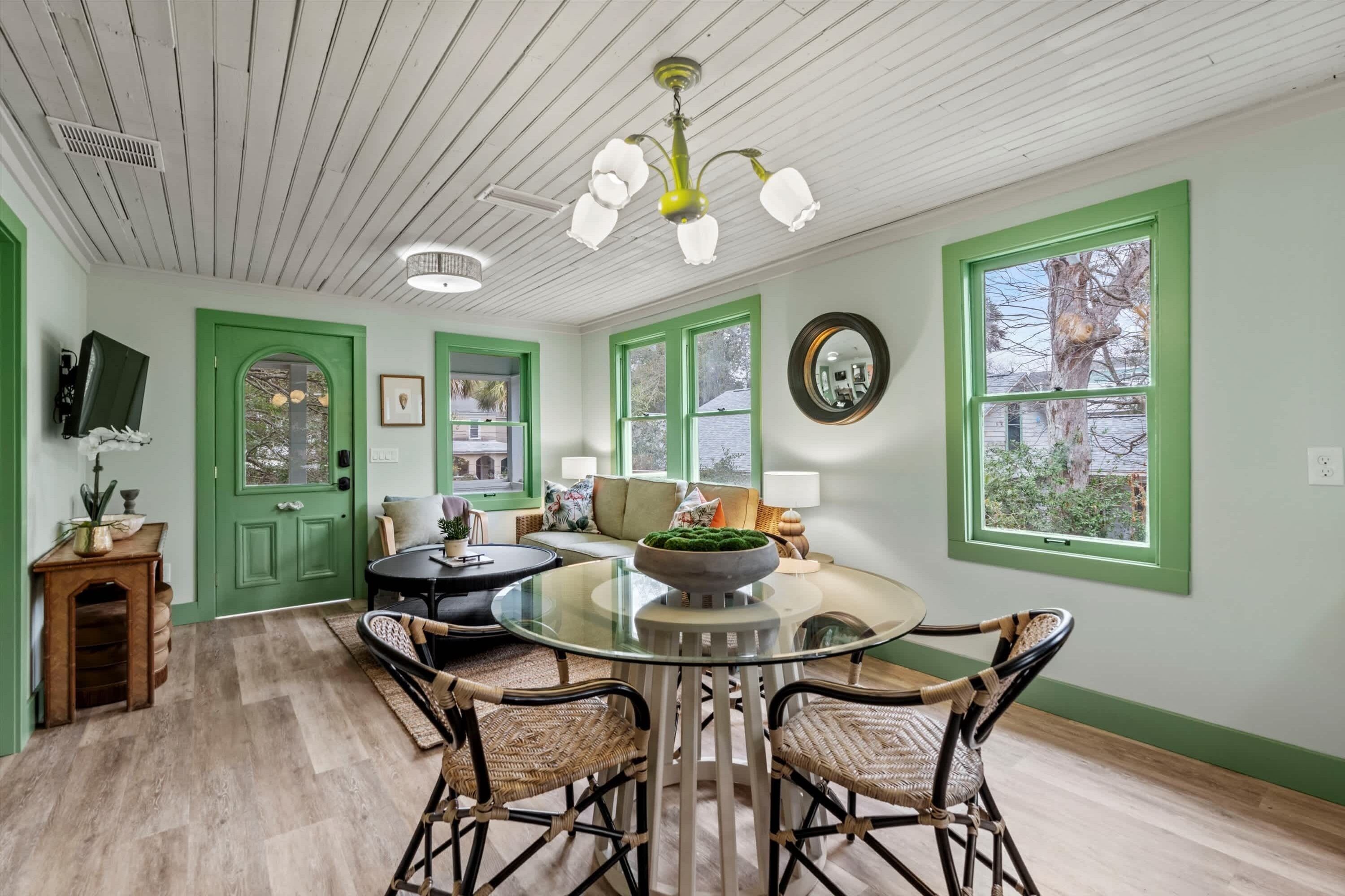 A dining area with a glass table, wicker chairs, and a green-framed window.