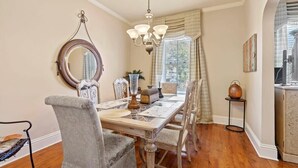 Uma sala de jantar com um candelabro, um espelho redondo e uma janela com cortinas.