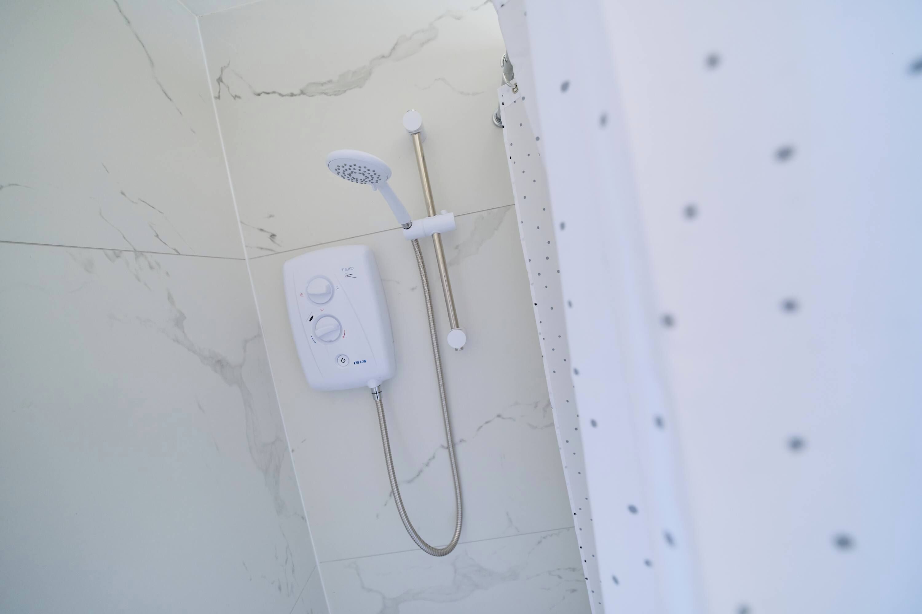 A shower with a handheld showerhead and a wall-mounted control panel.