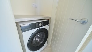 A compact washing machine in a small laundry room with a door and a light switch on the wall. - 3 Bed Foyle View House In Derry City With Parking (Derry/Londonderry)