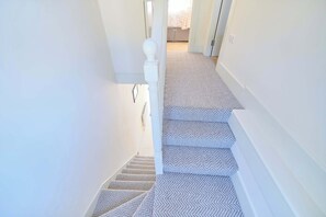 Eine Treppe mit einem gemusterten Teppich, weißen Wänden und einer weißen Brüstung.