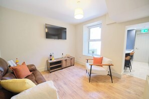 A living room with a sofa, armchair, TV, wooden cabinet, and a window. - 3 Bed Foyle View House In Derry City With Parking (Derry/Londonderry)