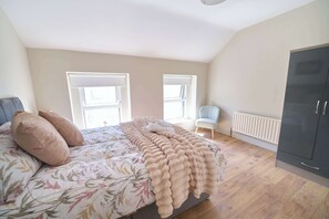 A bedroom with a bed, two windows, a chair, a radiator, and a wardrobe. - 3 Bed Foyle View House In Derry City With Parking (Derry/Londonderry)