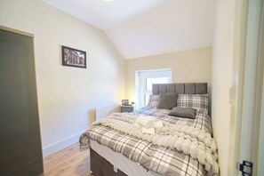 Ein Schlafzimmer mit Bett, Nachttisch, Fenster und Tür.