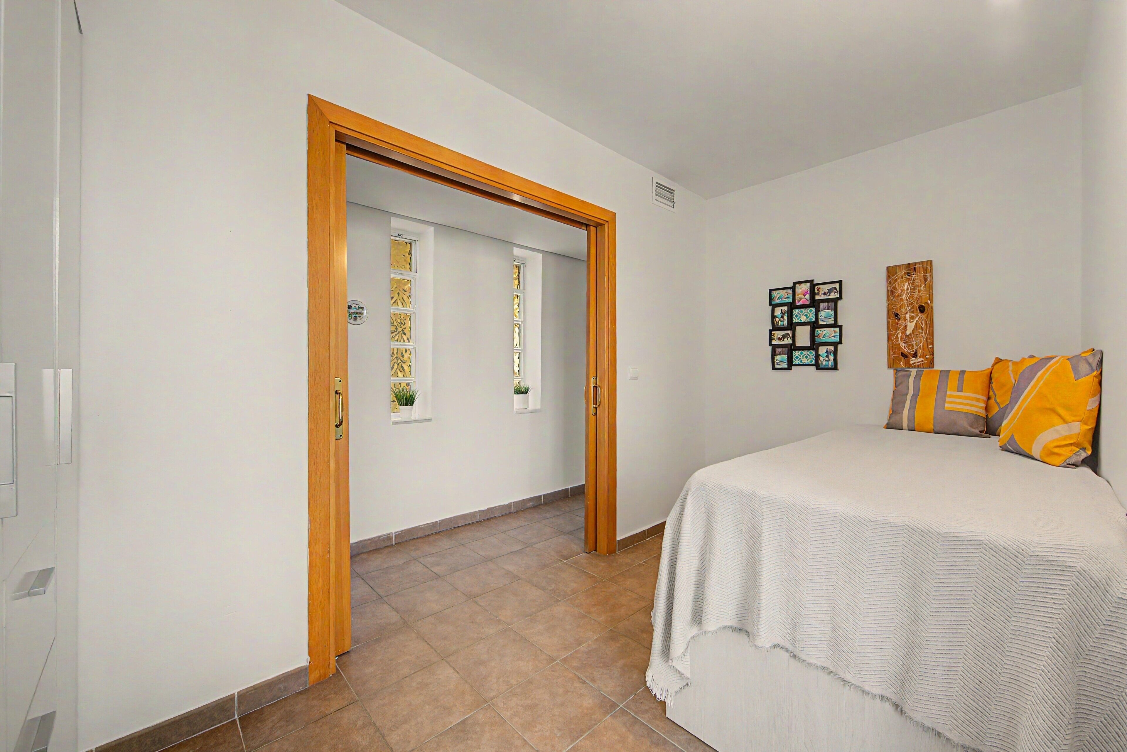 A bedroom with a bed, a door leading to another room, and a wall with framed pictures.