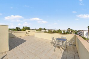 A rooftop terrace with a table and chairs, a tiled floor, and a view of the cityscape. - Apartment 'Ático Vacacional' with Shared Pool, Balcony and Air Conditioning (Almería)