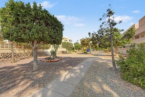 A paved walkway with gravel borders, surrounded by trees and a playground. - Apartment 'Ático Vacacional' with Shared Pool, Balcony and Air Conditioning (Almería)