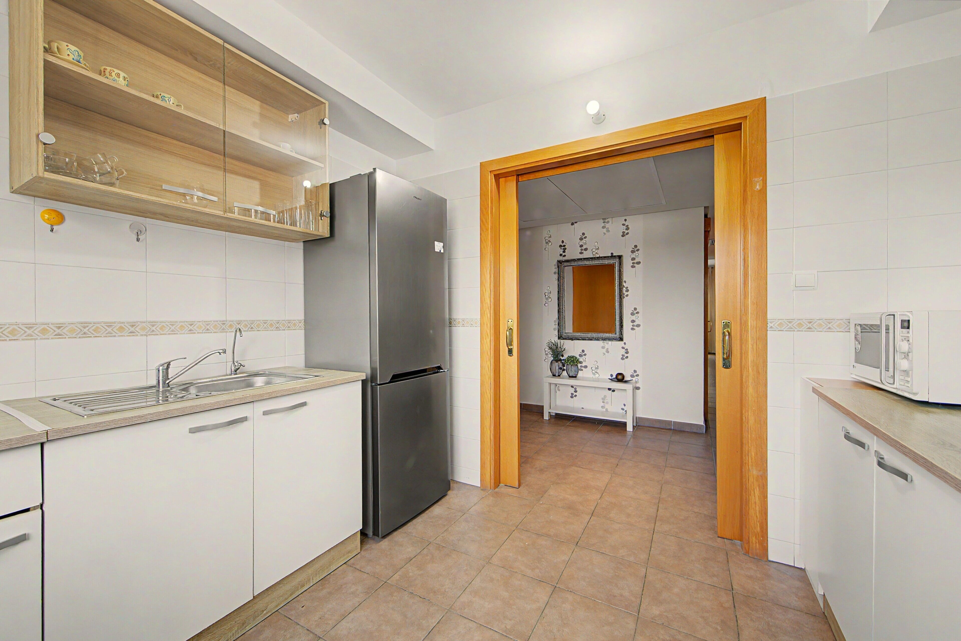 A kitchen with a stainless steel refrigerator, a sink, and a wooden cabinet with decorative items.