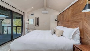 Een slaapkamer met een groot bed, een houten hoofdbord, een plafondventilator en uitzicht op het omliggende landschap.