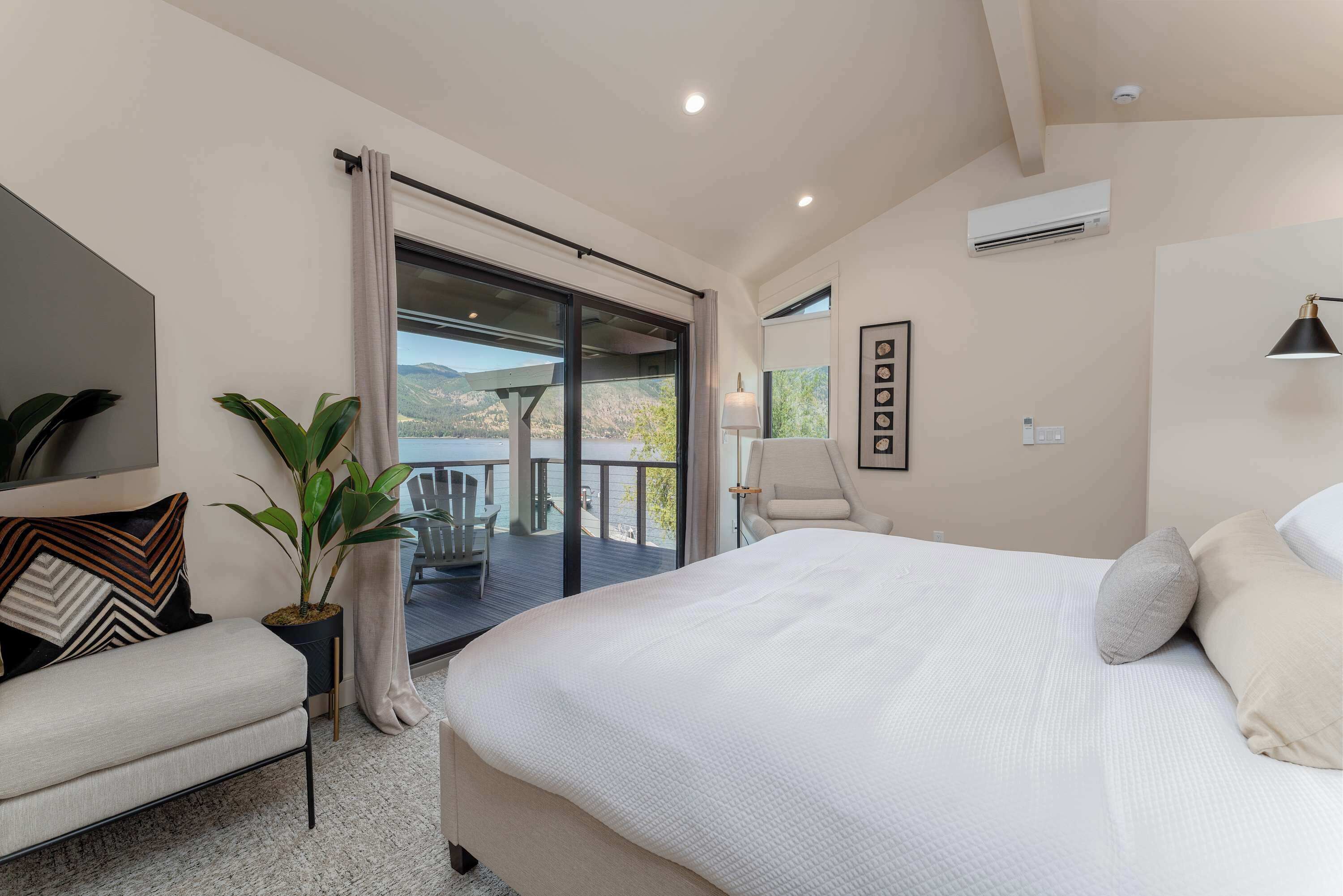 A bedroom with a large bed, a chair, a potted plant, and a balcony with a view.