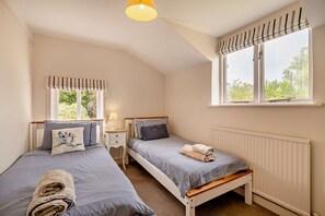 Ein Schlafzimmer mit zwei Einzelbetten, einem Fenster mit Vorhängen, einem Nachttisch mit Lampe und einer Heizung.