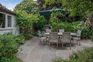 Eine Terrasse mit Tisch und Stühlen, umgeben von üppigem Grün und einem Steinweg.