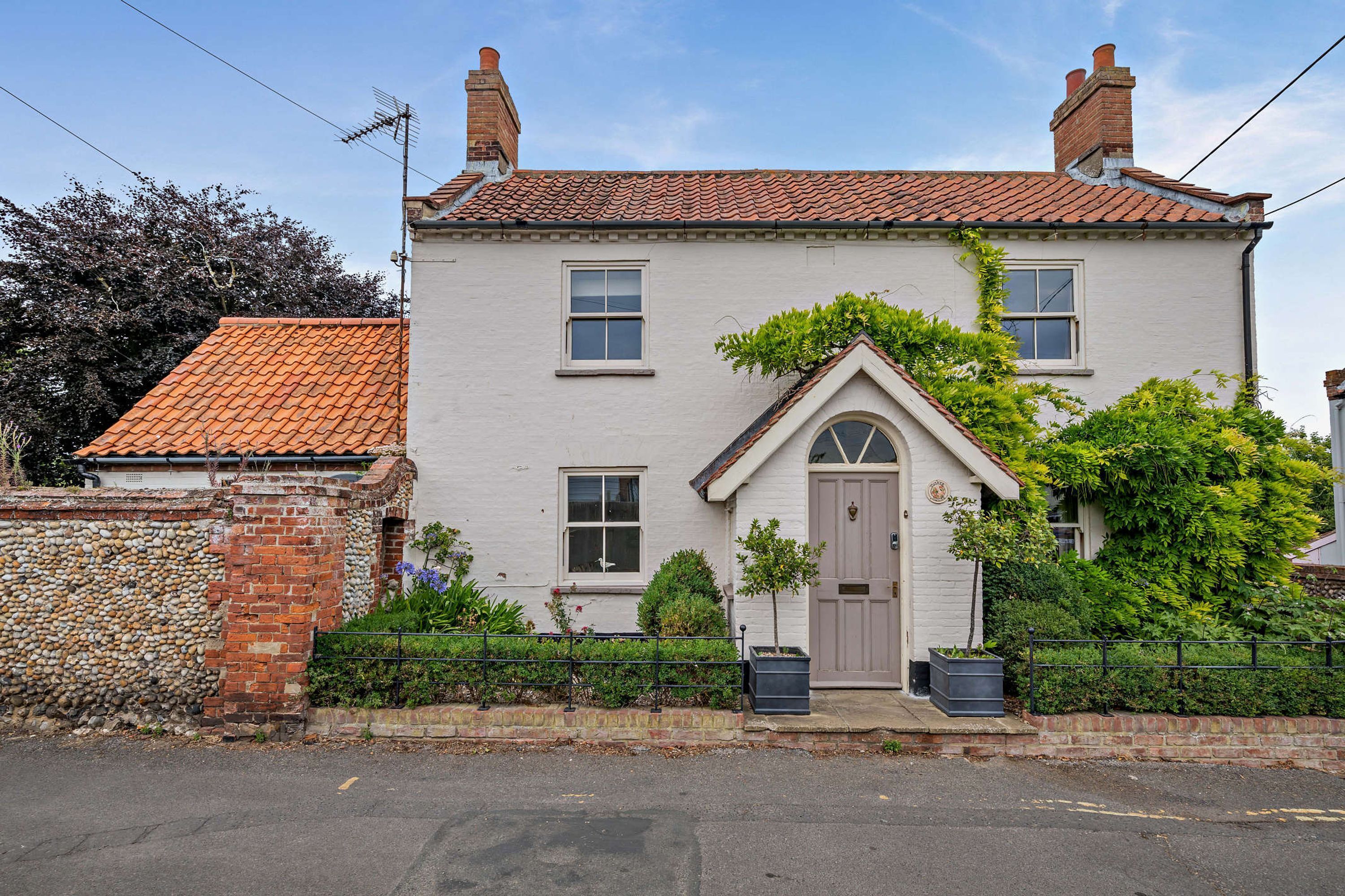 A two-story house with a tiled roof, a central door with a triangular pediment, and a small front garden.