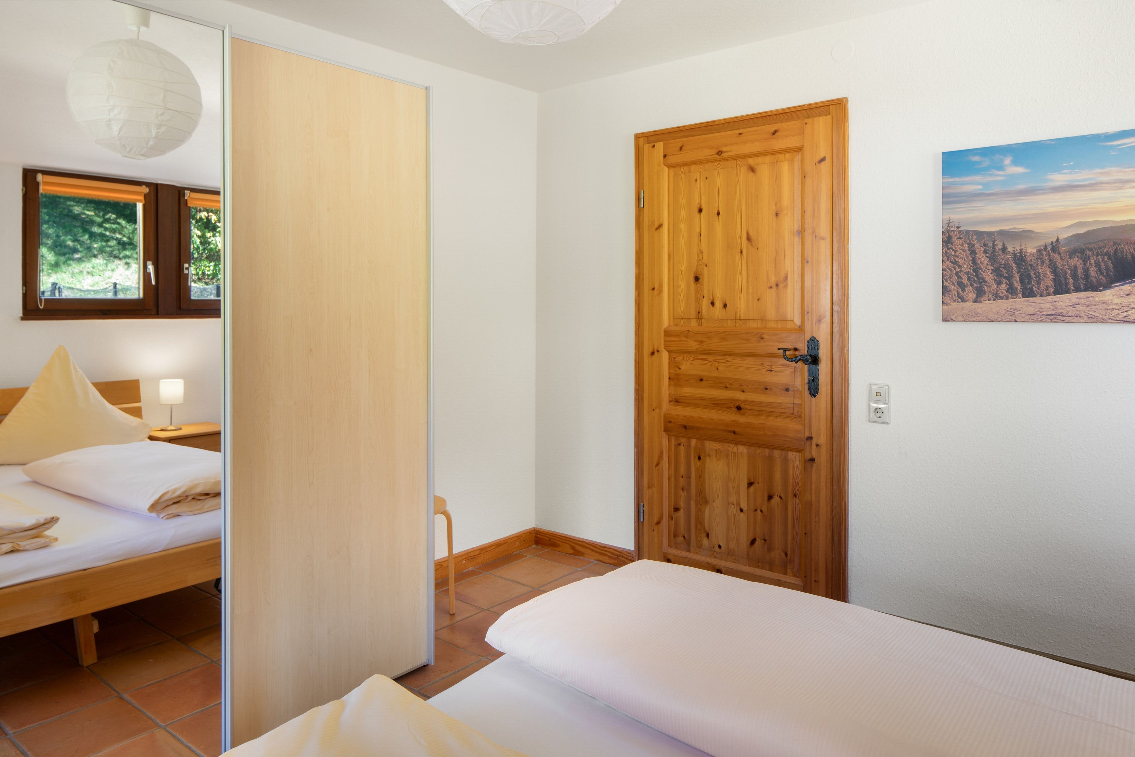 Un dormitorio con cama, una puerta de madera y ventana con vistas a árboles.