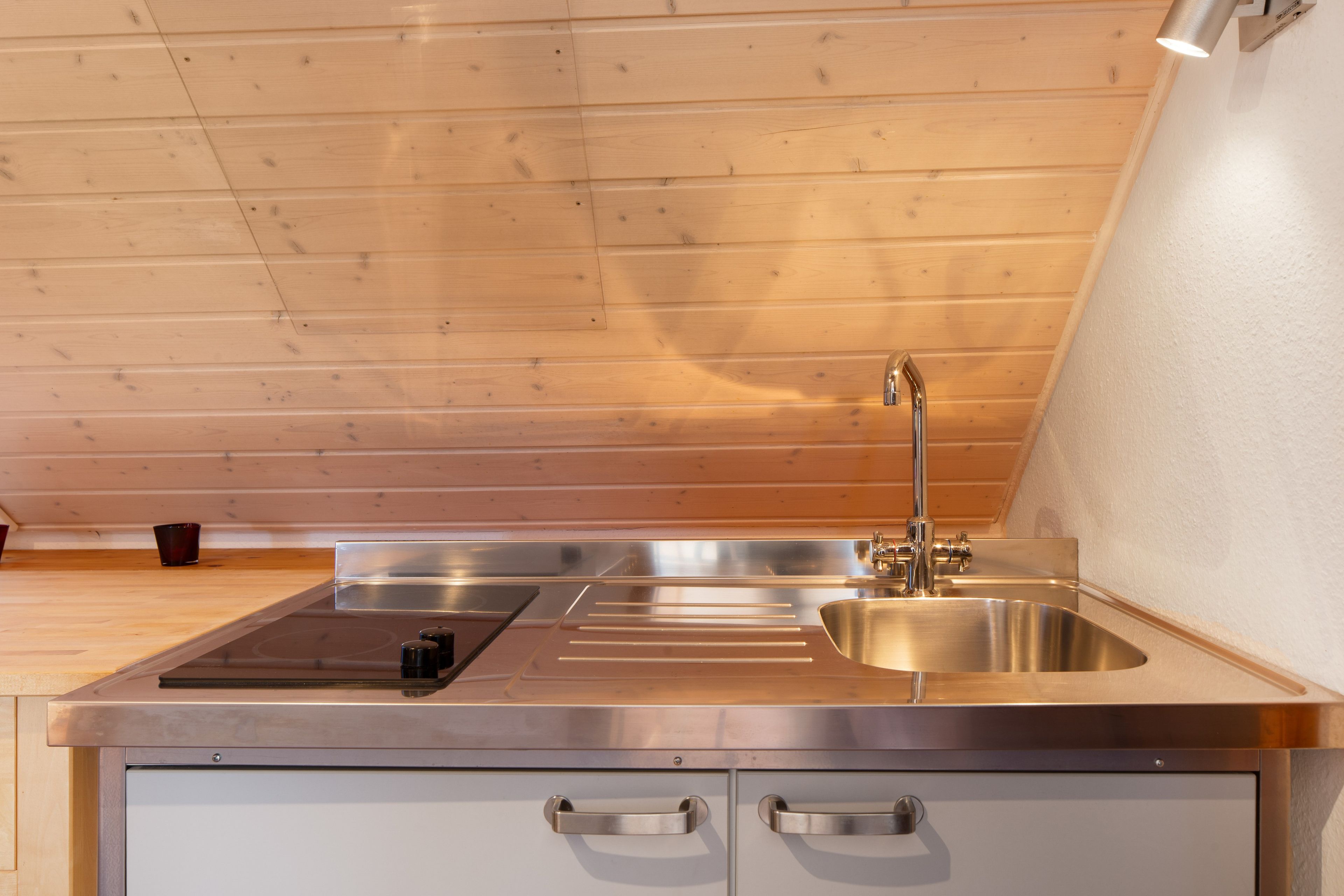 A modern kitchen with a stainless steel sink, a built-in stovetop, and a wooden ceiling.