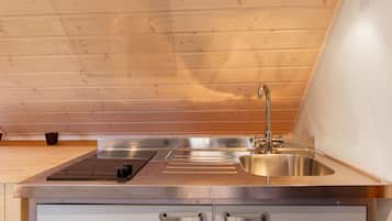 A modern kitchen with a stainless steel sink, a built-in stovetop, and a wooden ceiling.
