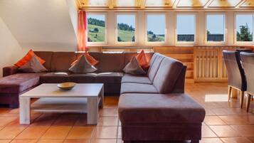Een moderne woonkamer met een modulaire bank, een salontafel en uitzicht op een groen landschap door grote ramen.
