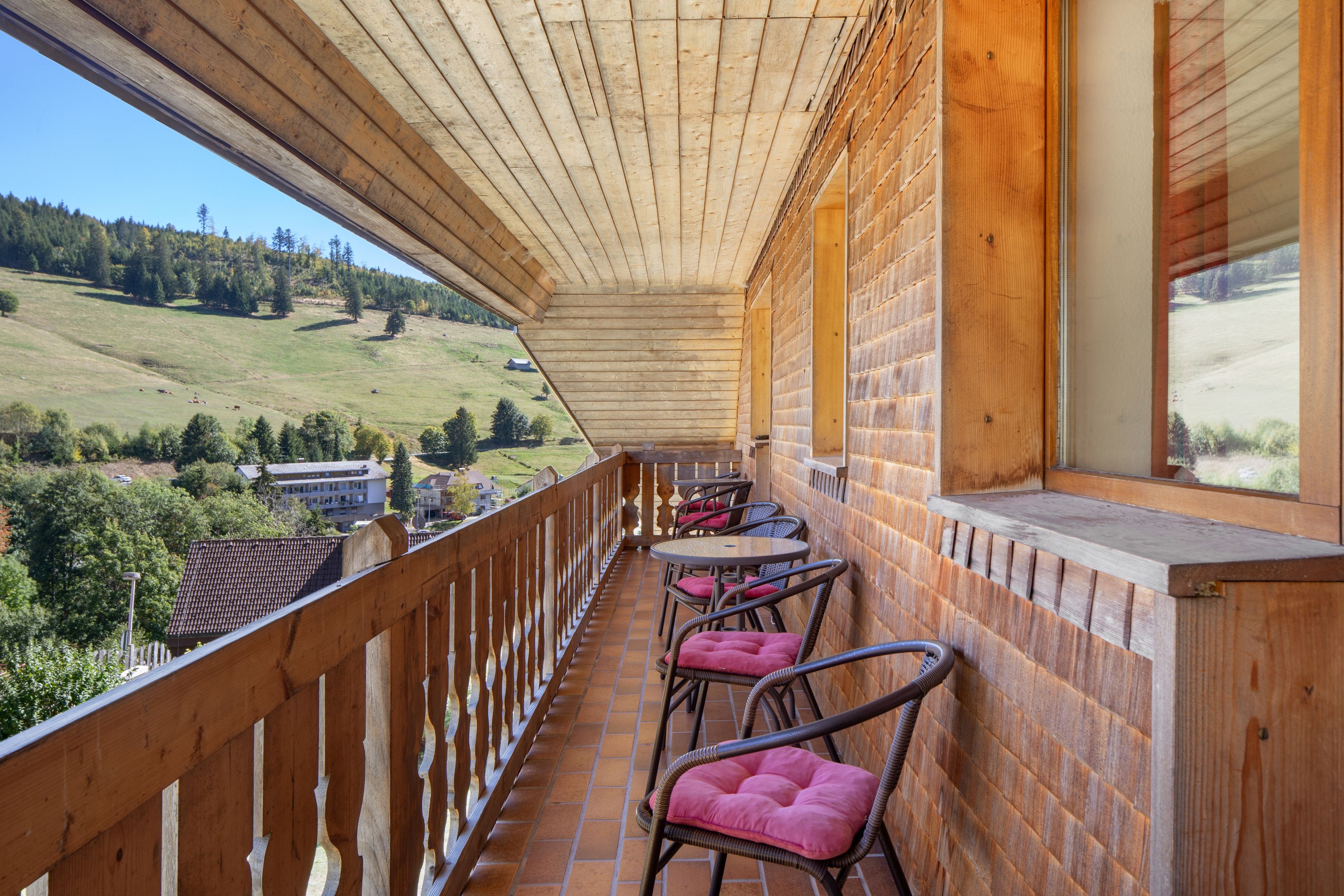 A wooden balcony with a view of a green landscape and buildings.