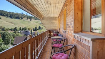A wooden balcony with a view of a green landscape and buildings.