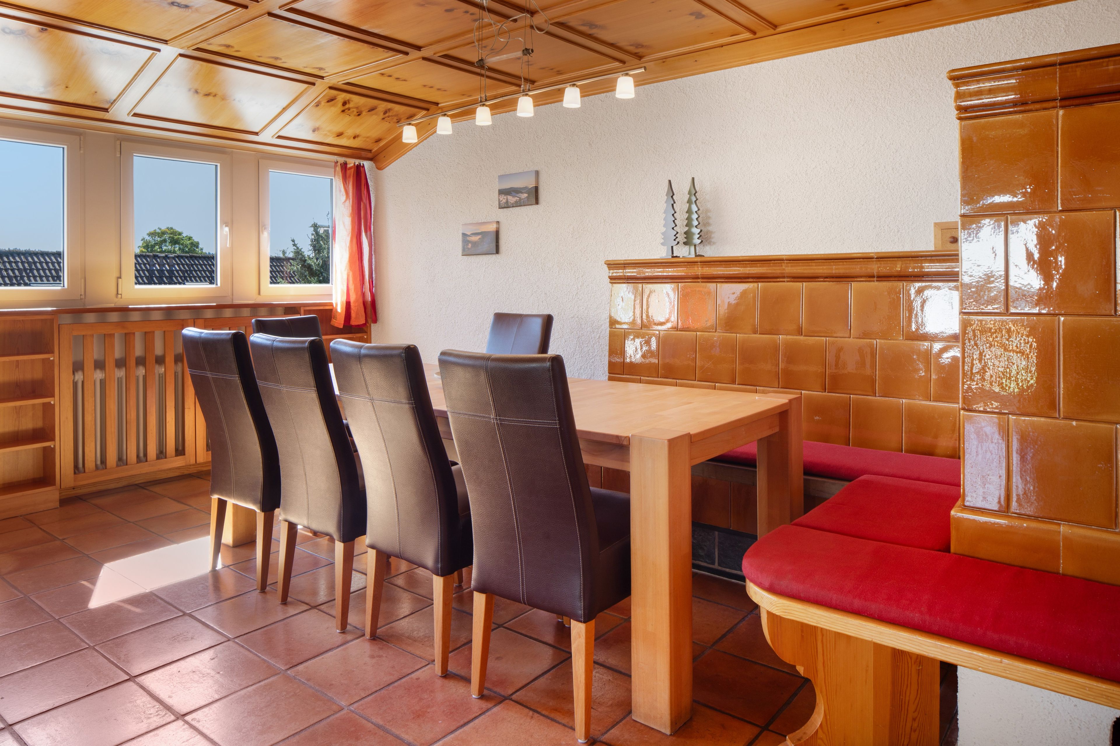 Un'area pranzo con un tavolo e sedie in legno, una panca imbottita rossa e vista all'esterno attraverso ampie finestre.