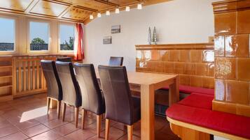 Un'area pranzo con un tavolo e sedie in legno, una panca imbottita rossa e vista all'esterno attraverso ampie finestre.