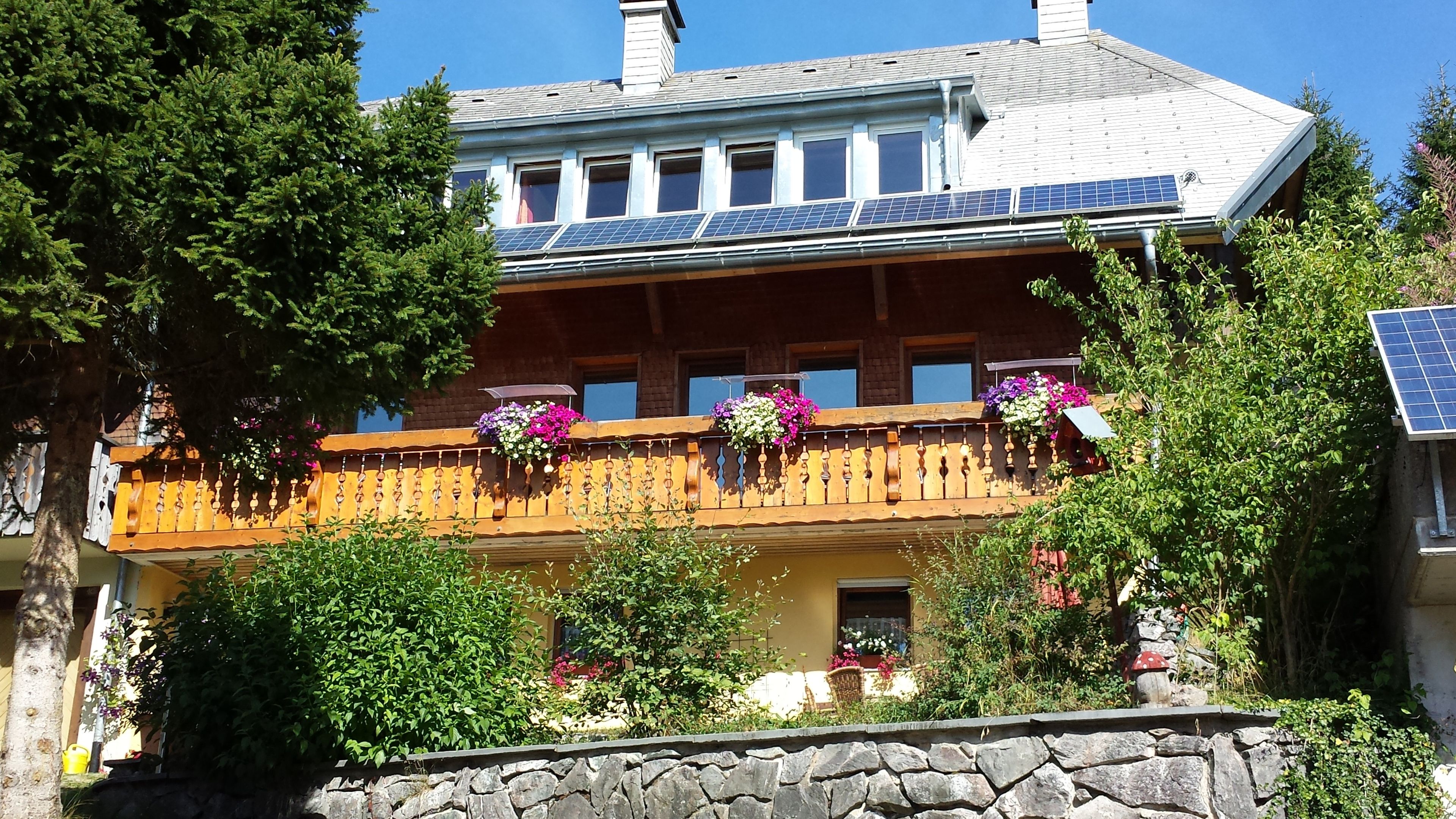 Ein zweistöckiges Gebäude mit Balkon, Steinmauer und Solaranlage.