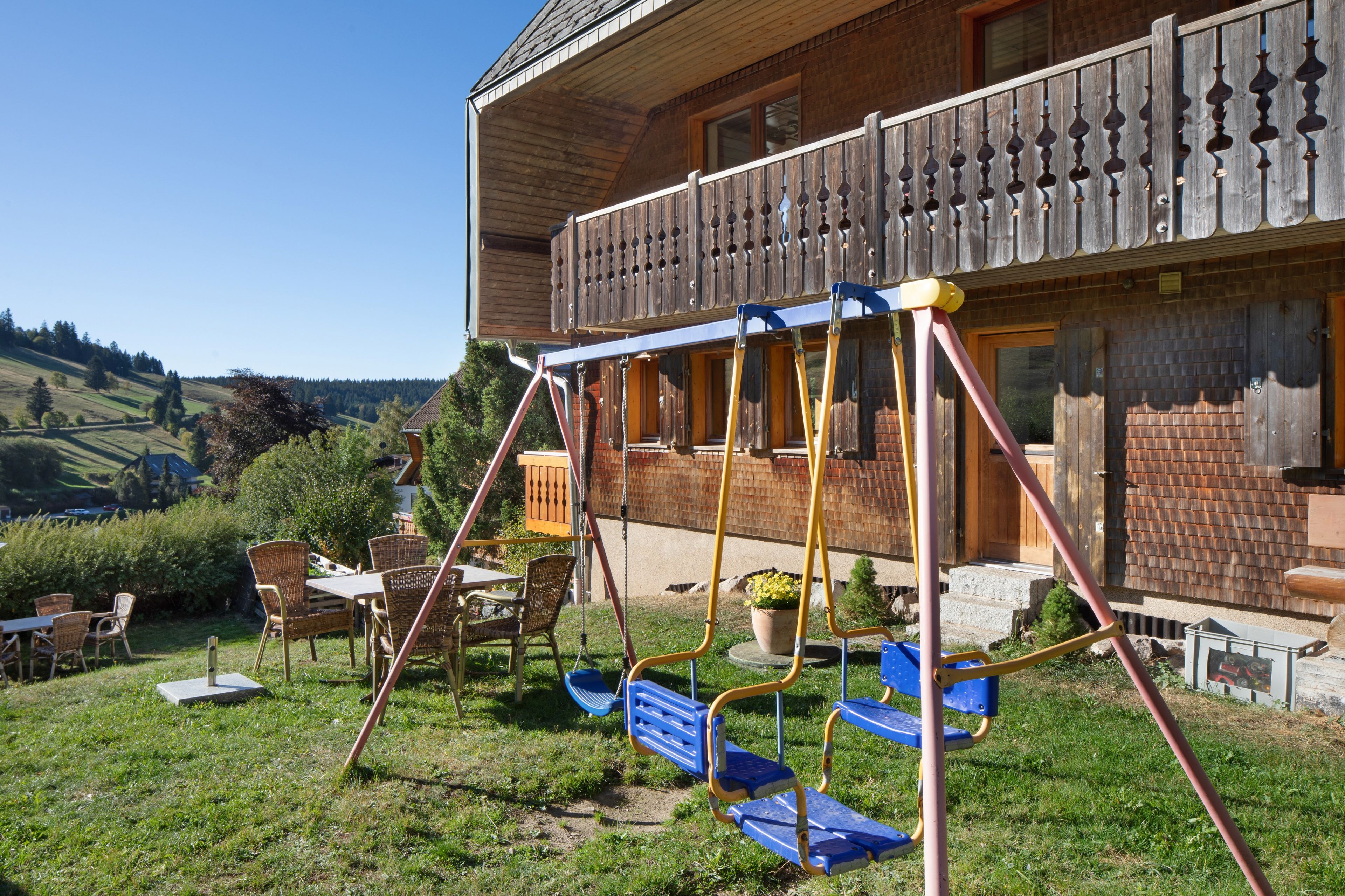 A wooden house with a balcony, a swing set, and a dining area with wicker furniture.