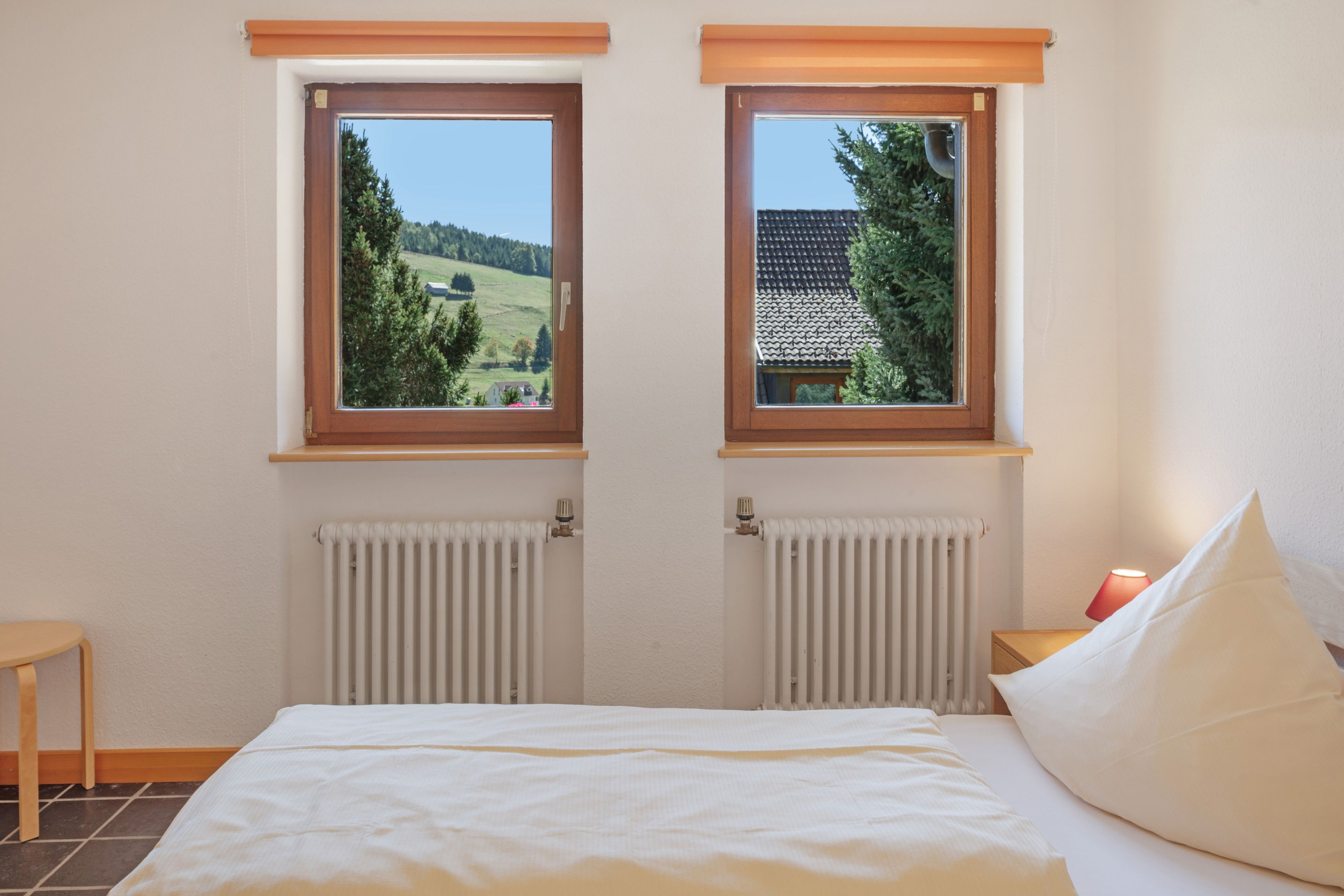 Ein Schlafzimmer mit zwei Fenstern, einem Bett, einem Nachttisch und einer Heizung.