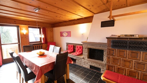 A dining area with a table set for four, a fireplace with a stone surround, and a window with curtains. - Apartment 4 at Gästehaus Bühlhof in Todtnauberg (Todtnau)