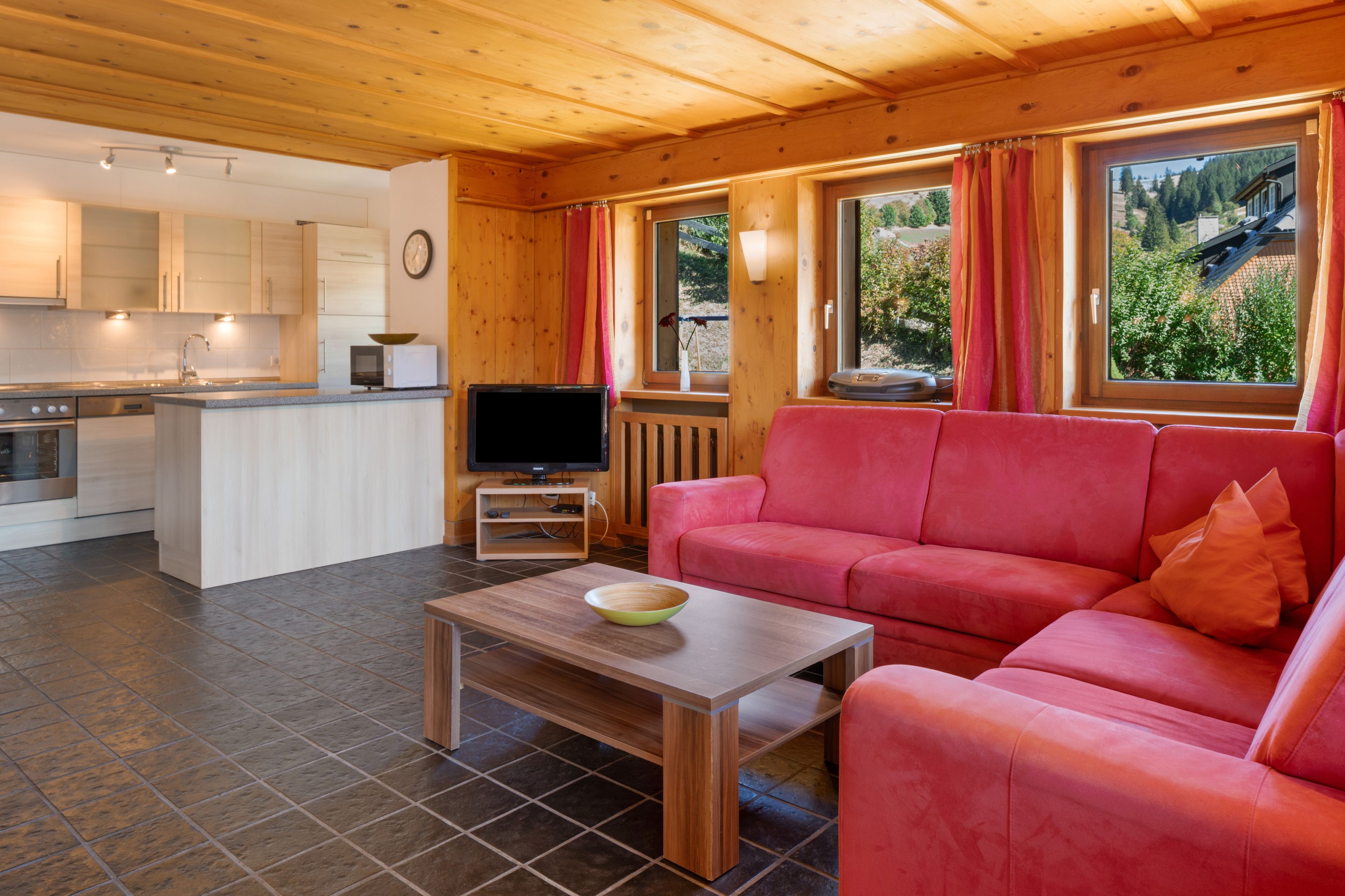 Een modern interieur met een keuken, een zithoek met een rode bank en een televisie.