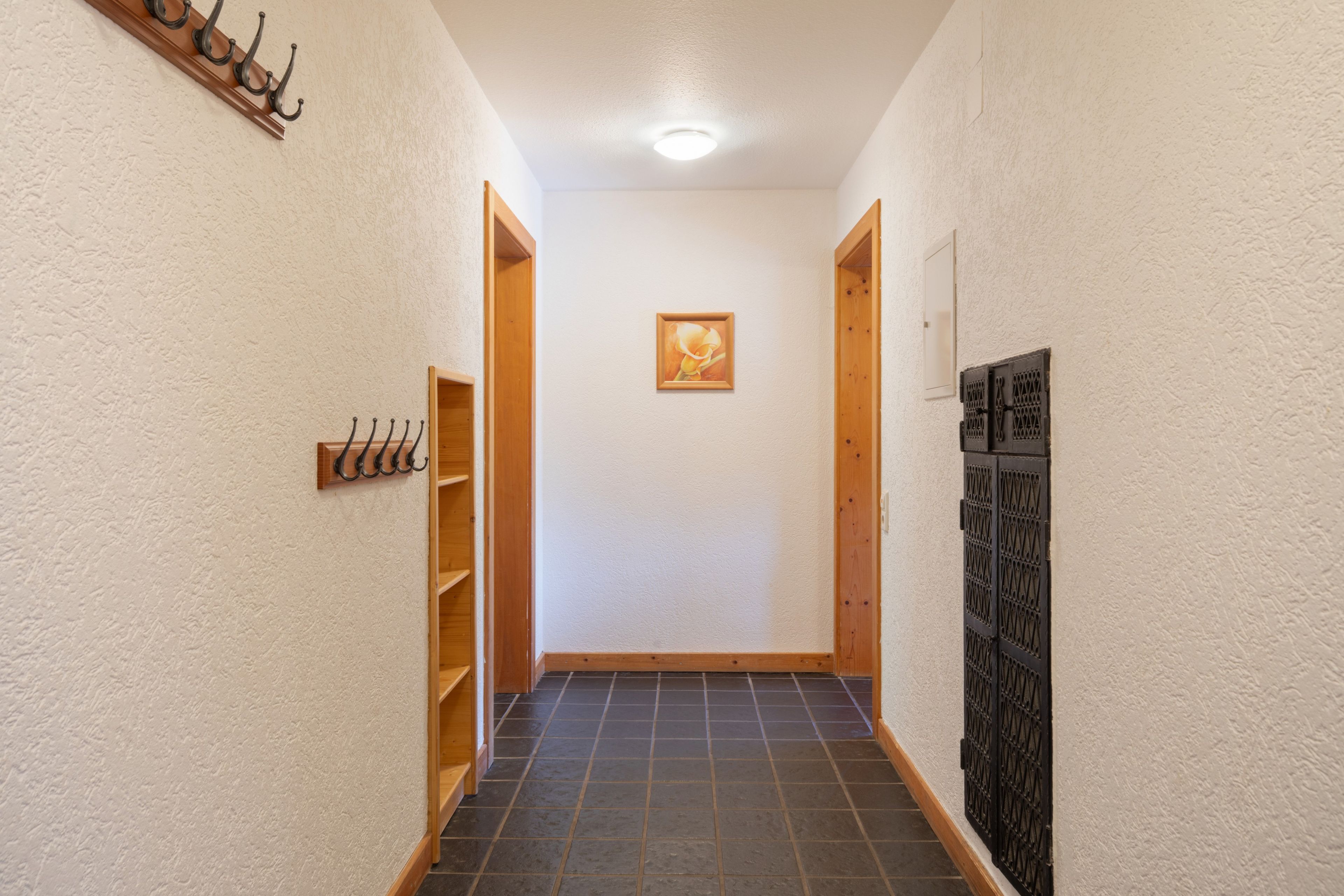 Ein schmaler Flur mit Fliesenboden, Holztüren und einem an der Wand hängenden Bild.