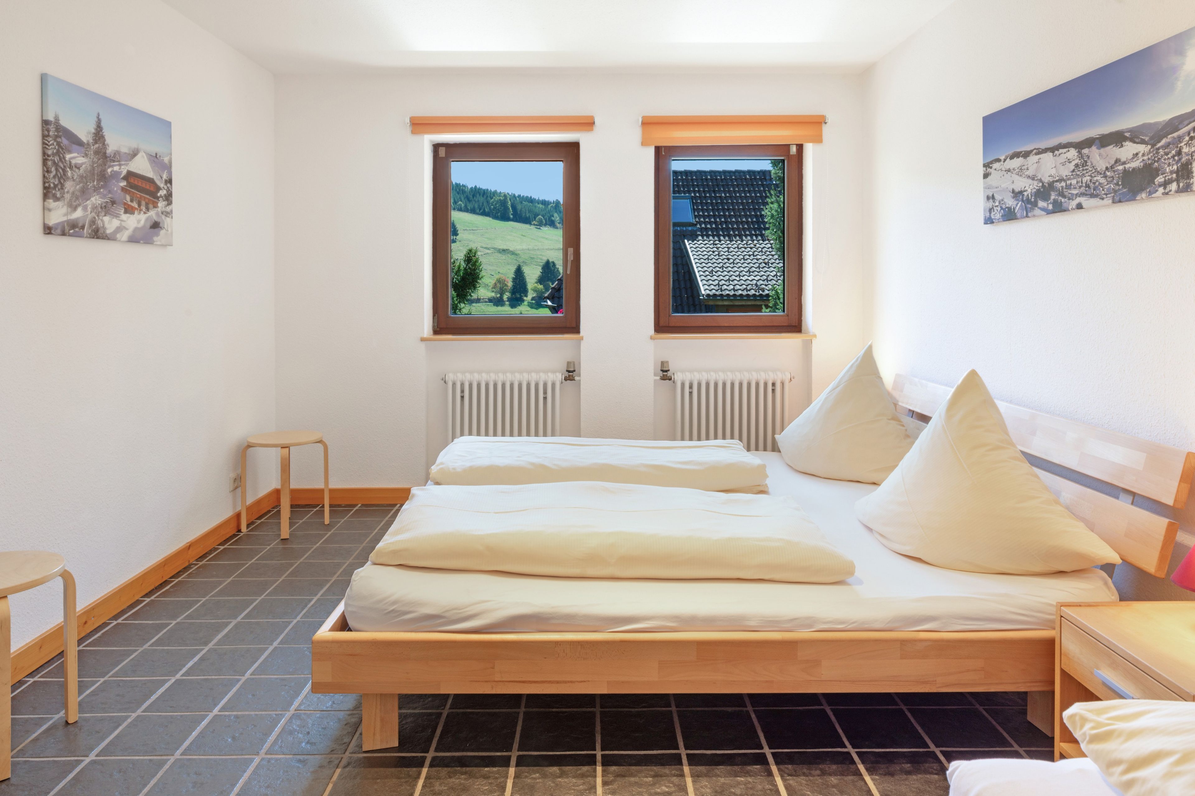Un dormitorio con dos camas, un taburete pequeño y dos ventanas que dan a un paisaje verde.