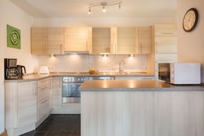 Une cuisine moderne avec des meubles en bois clair, des appareils en acier inoxydable et un îlot central.