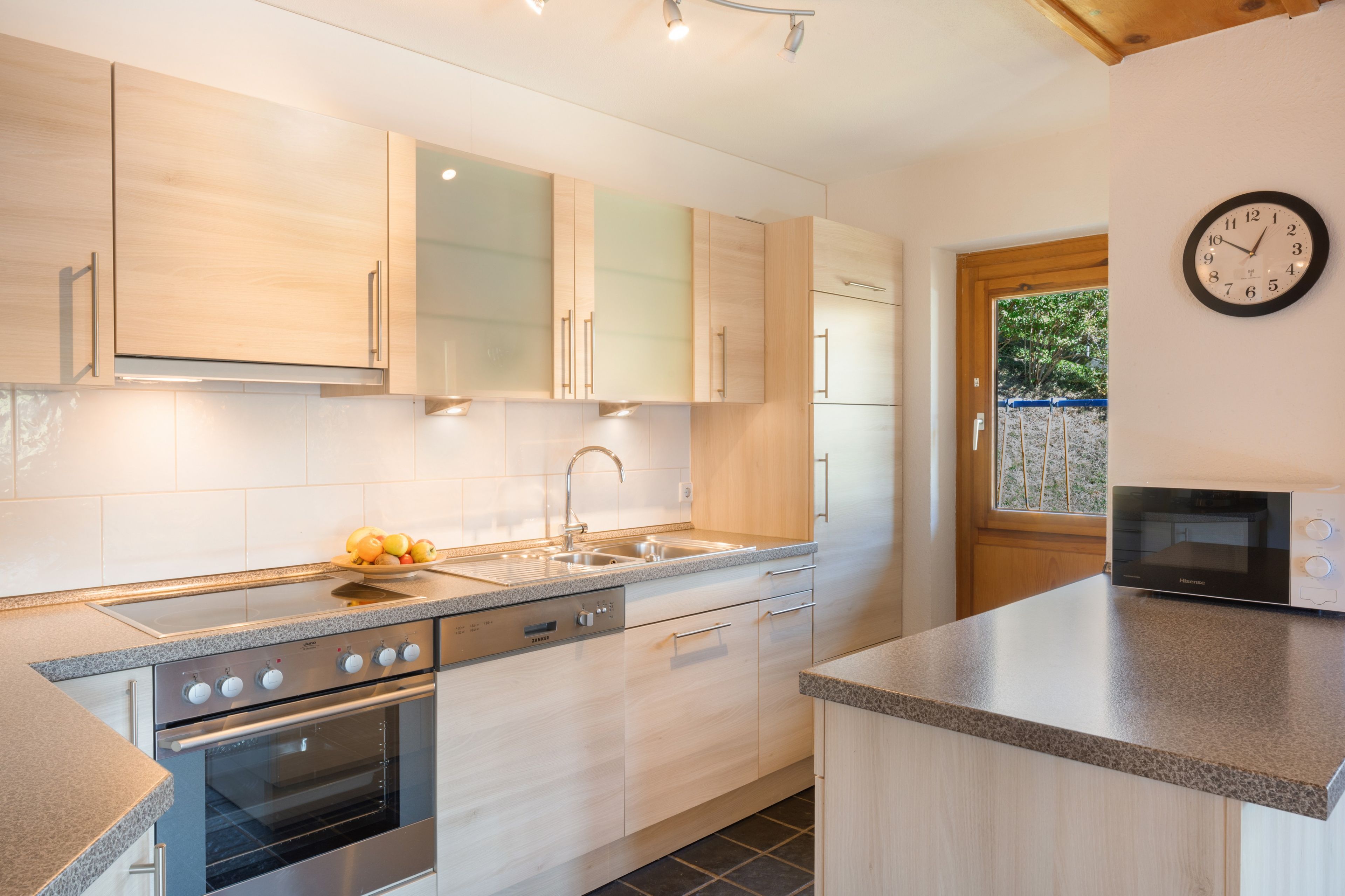 Una cocina moderna con armarios de madera clara, horno de acero inoxidable y microondas.