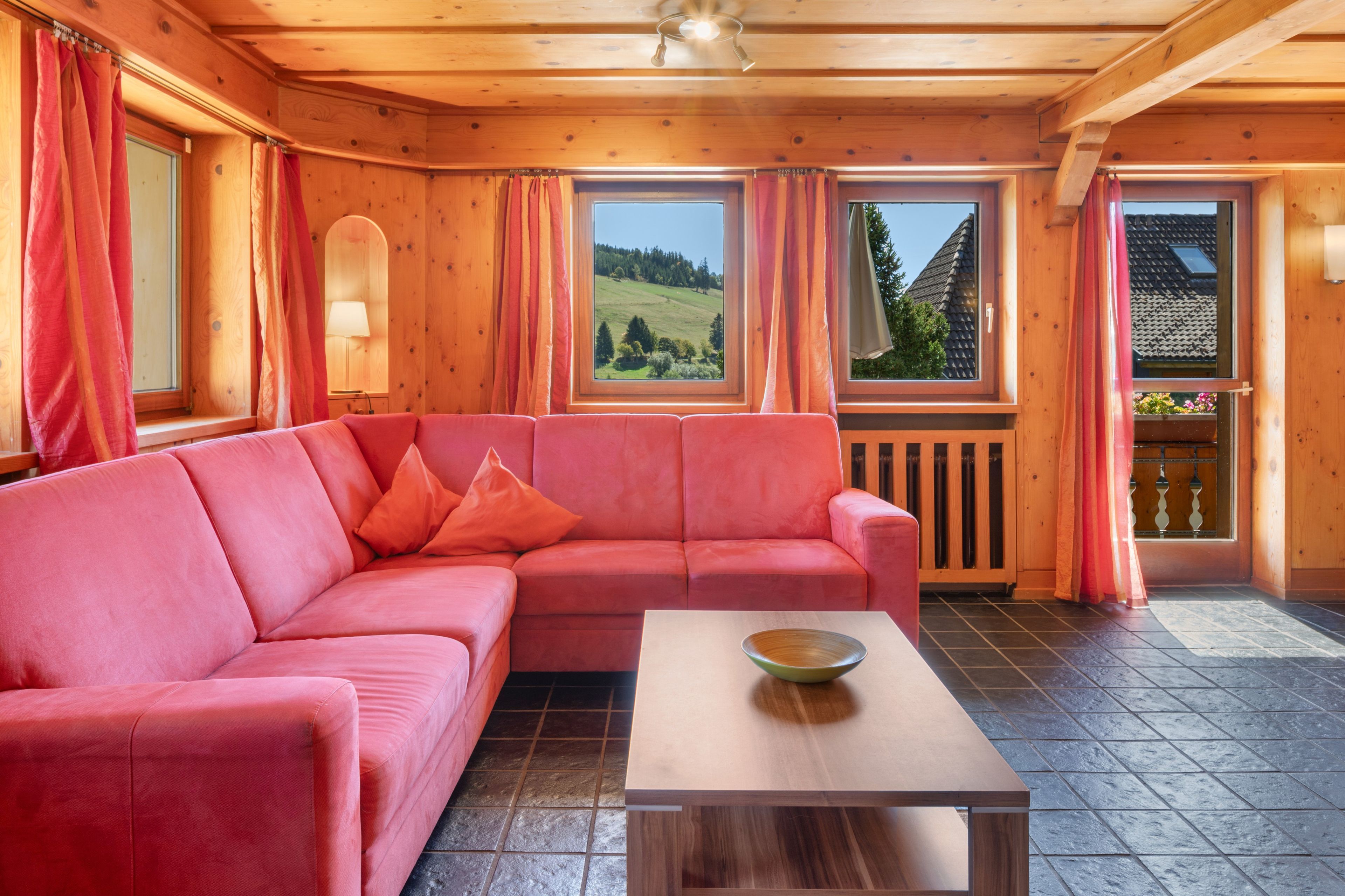Un interior de madera con un sofá rosa, una mesa de centro de madera y ventanas amplias con cortinas.