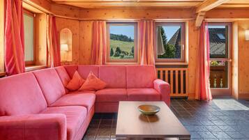 Un interior de madera con un sofá rosa, una mesa de centro de madera y ventanas amplias con cortinas.