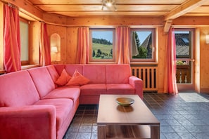 Un intérieur en bois avec un canapé rose, une table basse en bois et de grandes fenêtres avec des rideaux.