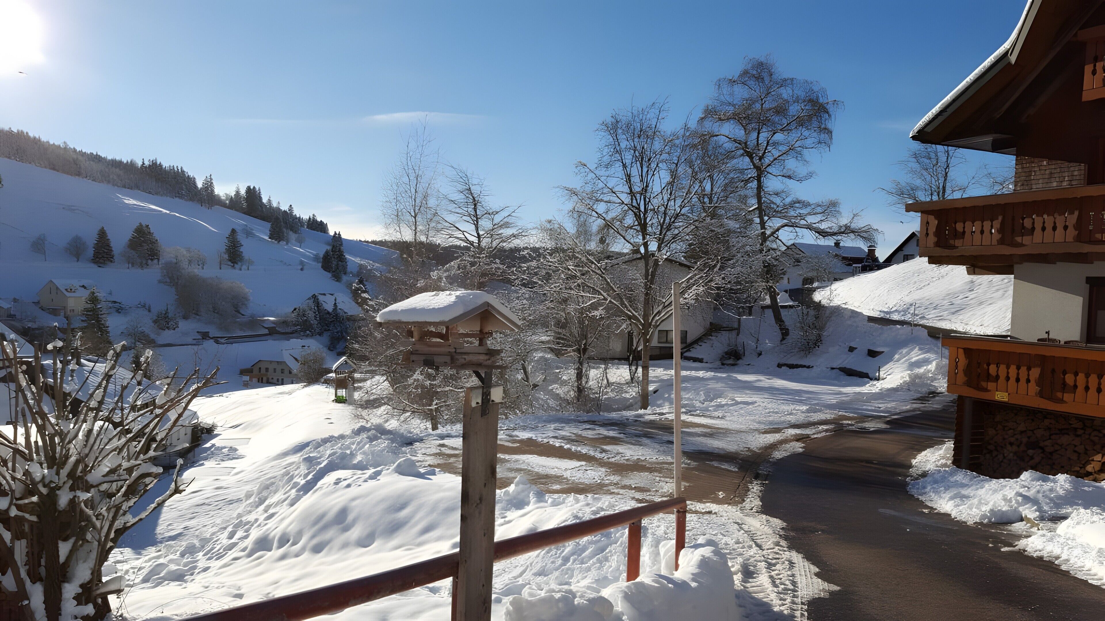 A snowy mountain village with wooden buildings, a snow-covered path, and a clear sky.