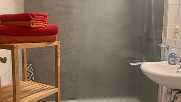 Une salle de bain avec une douche à parois de verre, une étagère en bois avec des serviettes, un lavabo et des toilettes.