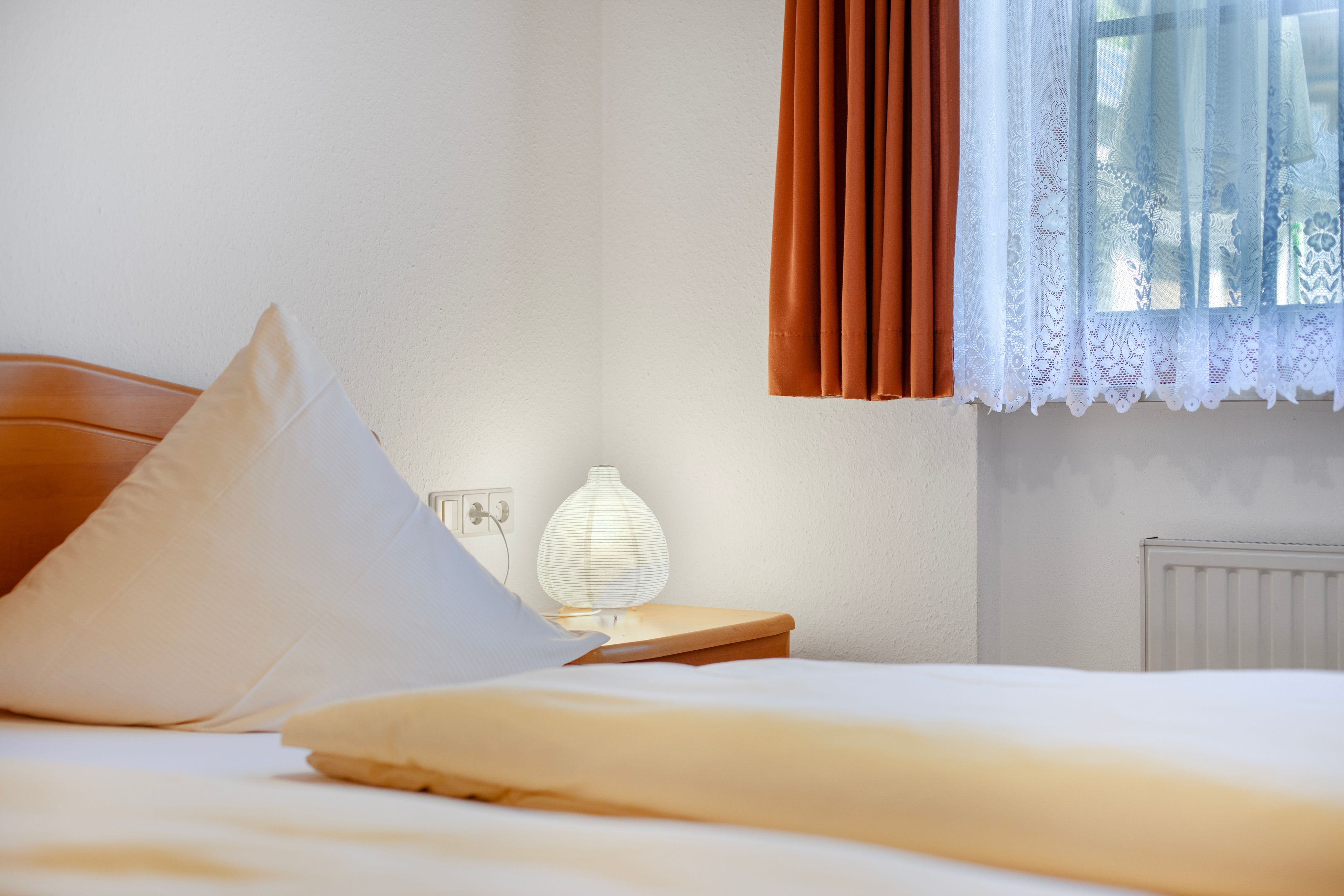 Una cama bien hecha con un cojín y una lámpara blanca sobre una mesita de noche.